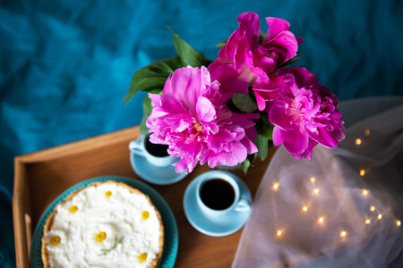 Coffee, pink peonies, cheesecake on a wooden tray, top viewの写真素材