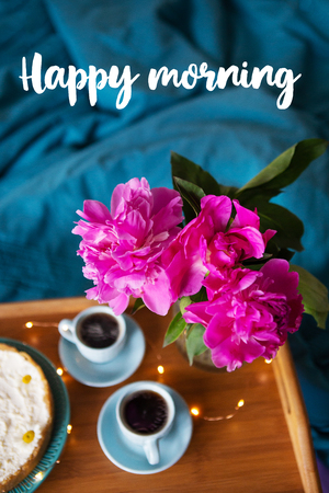 Coffee, pink peonies, cheesecake on a wooden tray, top view. Inscription happy morningの写真素材