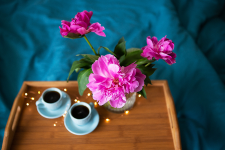 Coffee and pink peonies on a wooden tray in bed with bright linensの写真素材