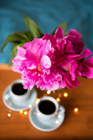 Coffee and pink peonies on a wooden tray in bed with bright bedding. Close-upの写真素材
