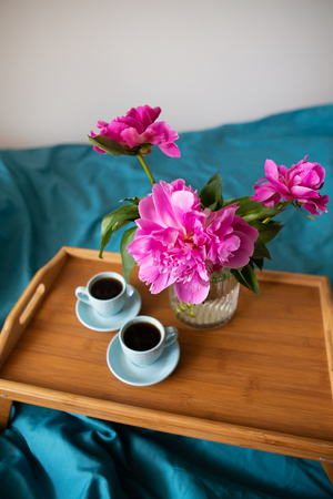 Coffee and pink peonies on a wooden tray in bed with bright linensの写真素材