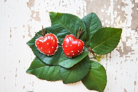 Beautiful and tasty dessert in the form of heart lies on green leaves on an old wooden background.の写真素材