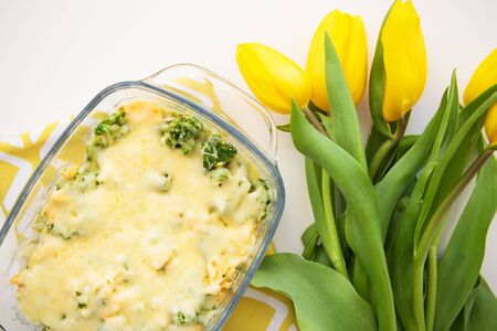 casserole with broccoli, cheese and cream on a background of yellow tulipsの写真素材