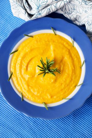 pumpkin cream soup in a blue plate on blue napkin with rosemaryの写真素材