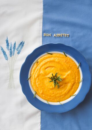 pumpkin soup in a blue plate with rosemary on a napkin with flowers, lettering bon appetitの写真素材