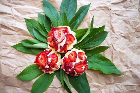Beautiful and bright cupcakes with strawberries lie on green leaves, close-up.の写真素材