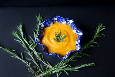 pumpkin soup in a blue plate on a black background with a branch of rosemaryの写真素材