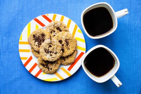 Oatmeal cookies with chocolate on blue napkin and two cups of coffeeの写真素材