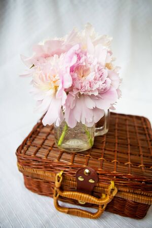 A very beautiful bouquet of pink peonies in a vase stands on a wooden suitcase. Beautiful composition.の写真素材