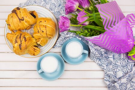 three croissants, two cups of coffee on the table and a bouquet of beautiful tulips.の写真素材