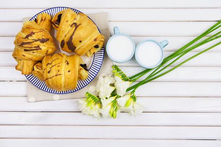 a beautiful breakfast-croissants on a plate and two cups of cappuccino, a bouquet of freesias.の写真素材
