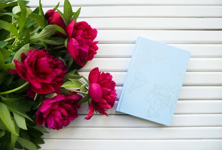 a bouquet of beautiful peonies lies on a white wooden table together with a blue bookの写真素材
