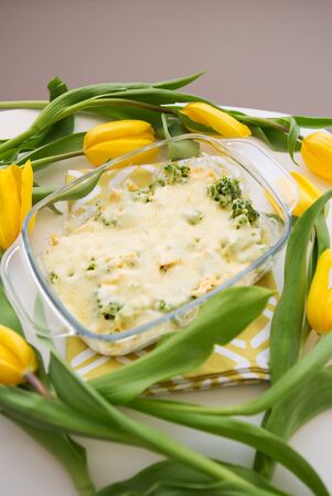 tasty casserole with broccoli, cheese and cream on a background of yellow tulipsの写真素材