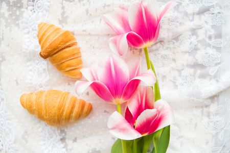 Three croissants and bright pink tulips on lace tablecloth, close-up.の写真素材