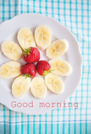 banana and strawberries on a white plate inscription good morningの写真素材