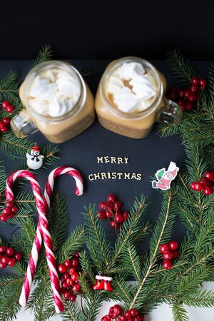 Candies and cocoa with marshmallows on a black background with the branches of trees. The inscription Merry Christmas.の写真素材