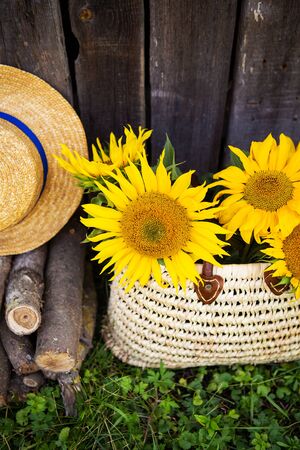 Logs, a hat, a bouquet of sunflowers in a straw bag are standing near a wooden house. Close-up.の写真素材