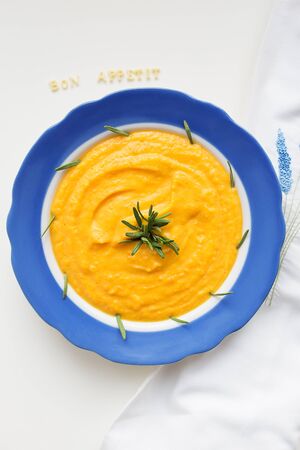 pumpkin soup in a blue plate on a napkin with flowersの写真素材