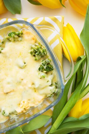 tasty casserole with broccoli, cheese and cream on a background of yellow tulipsの写真素材