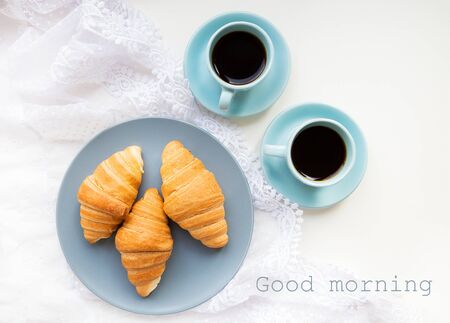 two cups of coffee with croissants on the background of lace inscription good morningの写真素材