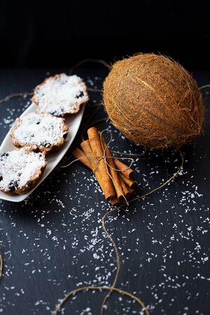coconut muffins on a white plate with whole coconut and cinnamon sticksの写真素材