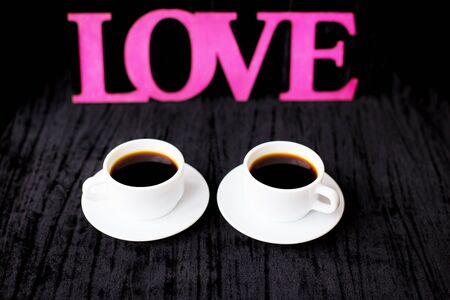two cups of coffee on pink background inscription love.の写真素材