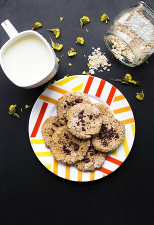 Oatmeal cookies with chocolate on a plate with colorful cup milkの写真素材