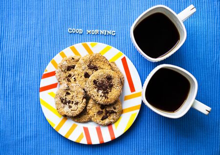 Oatmeal cookies with chocolate on blue napkin and two cups of coffee, good morning inscriptionの写真素材