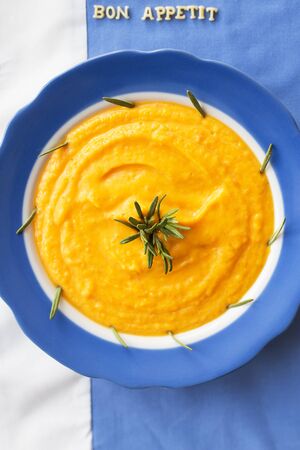 pumpkin soup in a blue plate with rosemary on a napkin with flowers, lettering bon appetitの写真素材
