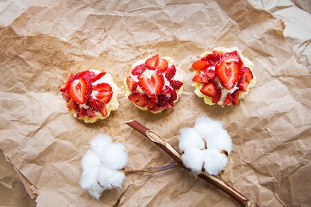 Beautiful cupcakes with strawberries along with a branch of cotton lies on kraft paper.の写真素材