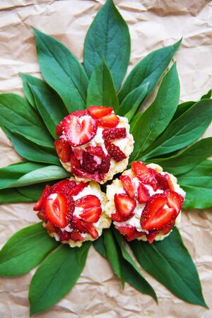 Beautiful and bright cupcakes with strawberries lie on green leaves, close-up.の写真素材