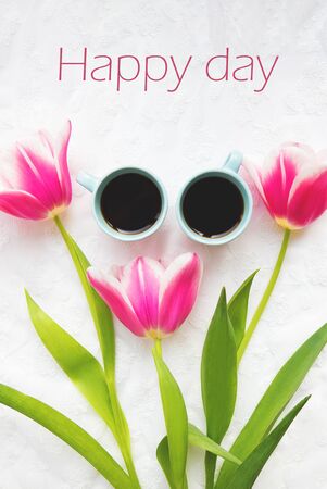 two cups of coffee and three beautiful pink tulips, inscription happy day.の写真素材