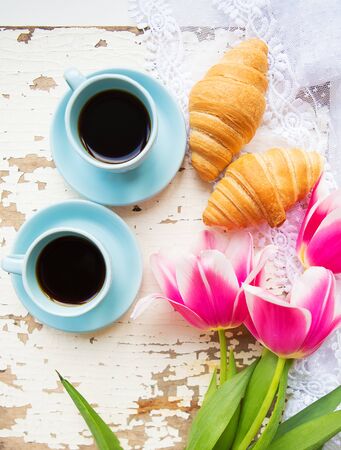 nice cup of coffee, croissants and pink tulips on old white table.の写真素材