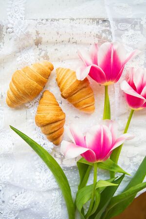 Three croissants and bright pink tulips on lace tablecloth.の写真素材