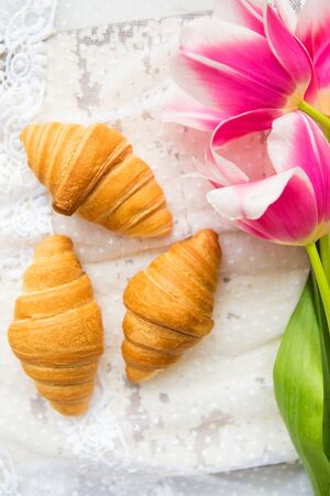 Three croissants and bright pink tulips on lace tablecloth, close-up.の写真素材