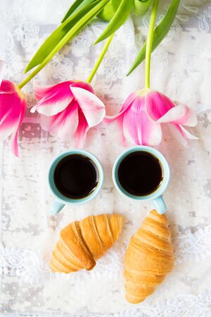 nice cup of coffee, croissants and pink tulips on old white table, close-up.の写真素材