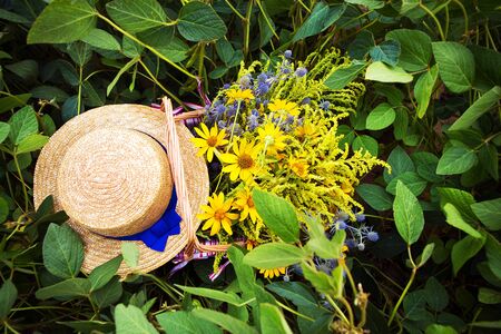 straw hat and basket with flowers stand on the grass, close-up.の写真素材