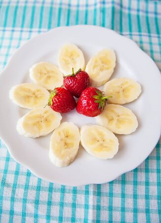 banana and strawberries on a white plate and a colorful napkinの写真素材