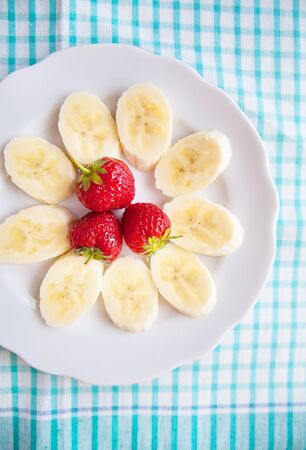 banana and strawberries on a white plate and a colorful napkinの写真素材