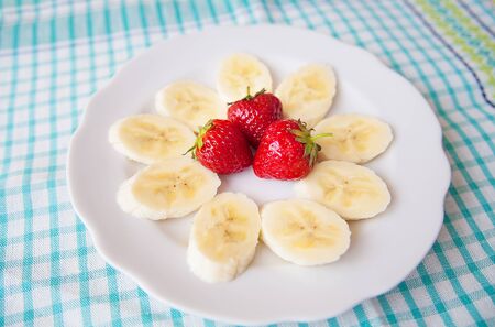 banana and strawberries on a white plate and a colorful napkinの写真素材