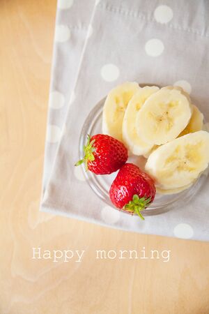 strawberry and banana on a glass plate on a wooden background, lettering happy morningの写真素材