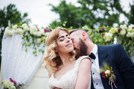 groom kisses the bride against the background of a floral arch in nature, rustic style.の写真素材