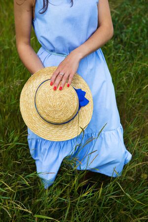 beautiful girl in a blue dress in the field holds a hat in her hands.の写真素材