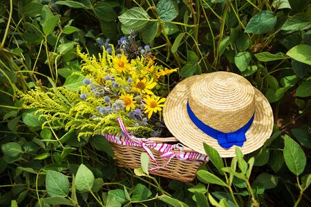 straw hat and basket with flowers stand on the grass.の写真素材