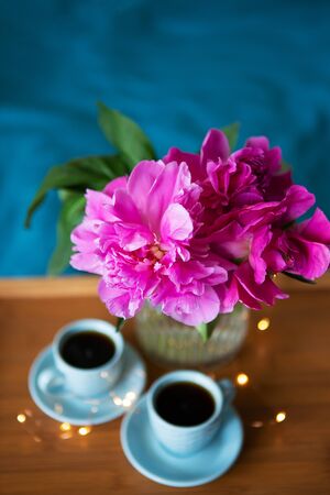 Beautiful pink peonies and two cups of coffee are standing on a wooden tray in bed. Close-up. Beautiful morning.の写真素材