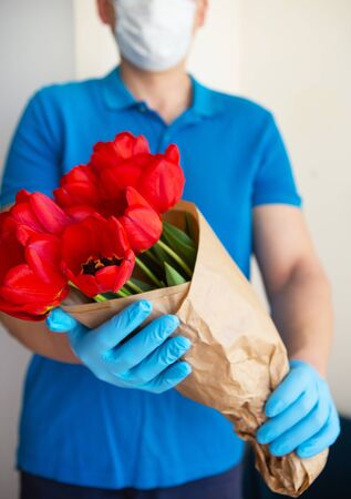 Contactless flower delivery by courier in a protective mask, medical gloves with a bouquet of red tulips. Close-up.の写真素材