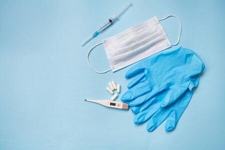 Blue latex gloves on a blue background lie with pills, medical mask, thermometer and syringe. The concept of health and self-control for viruses and epidemicsの写真素材