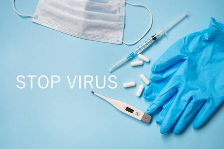 Blue latex gloves on a blue background lie with pills, medical mask, thermometer and syringe. Health and self-control concept for viruses and epidemics. The inscription stop virus.の写真素材