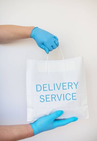 Contactless home shopping delivery with gloves holding a paper bag with food isolated on white background. The concept of quarantine and isolation during the coronavirus pandemic.の写真素材