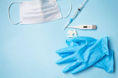 Blue latex gloves on a blue background lie with pills, medical mask, thermometer and syringeの写真素材